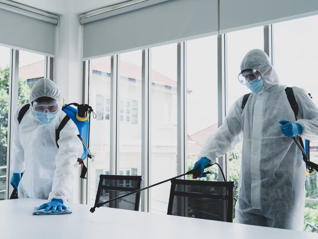 Disinfecting Cleaning Services Professional cleaners wearing a hazmat-like suit, disinfecting a table in office space.