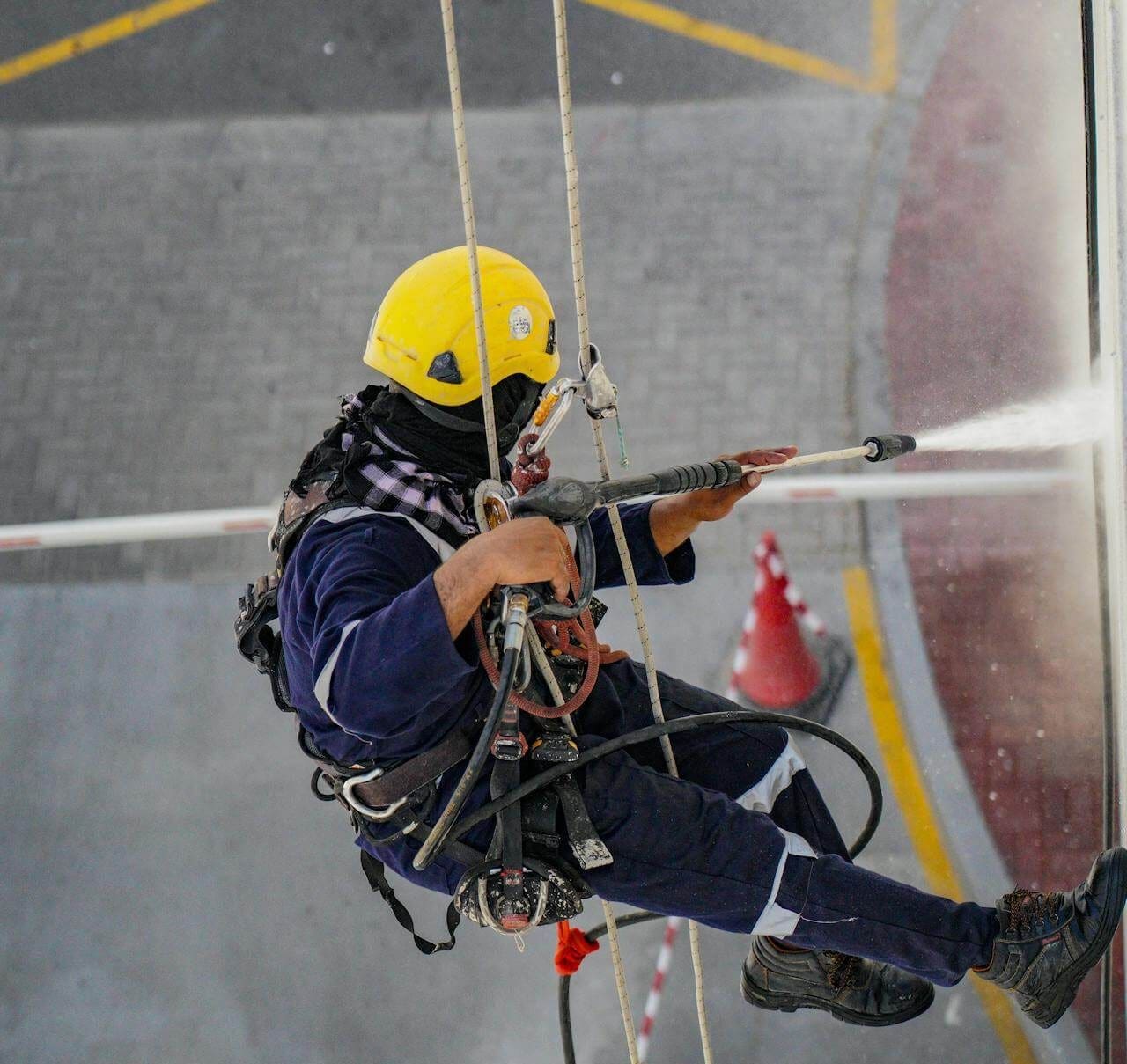guy suspended from a harness, using a power washer to clean what looks like a building's exterior guy suspended from a harness, using a power washer to clean what looks like a building's exterior