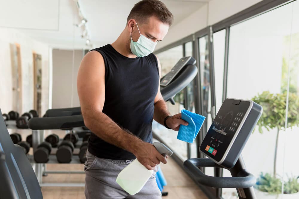 man sanitizing a treadmill in a gym