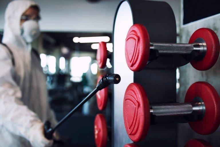 man disinfecting dumbbell racks